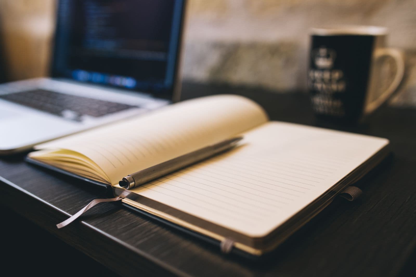 Open notebook and pen beside a laptop on a desk