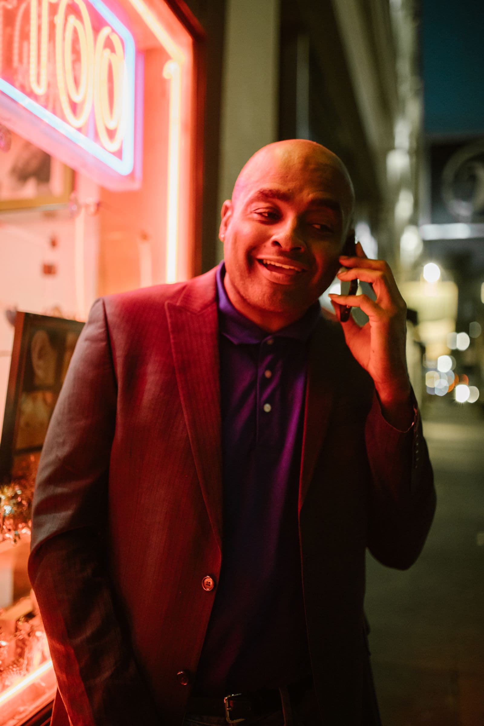 Business owner taking a phone call at night beside a neon sign